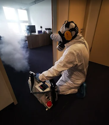 Techniker in Schutzkleidung mit Atemschutz und Vernebler im Innenraum